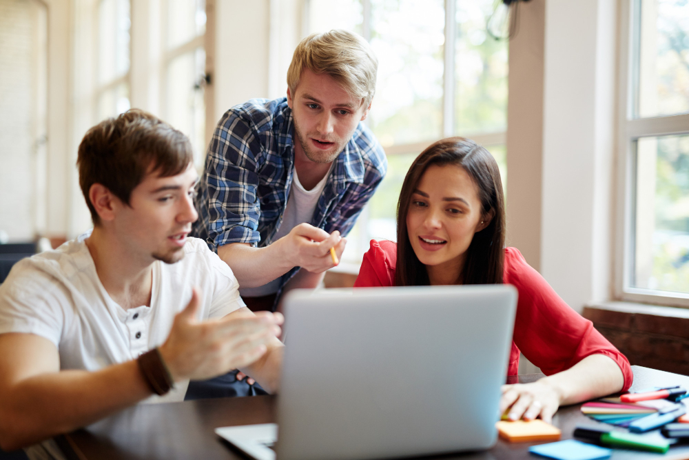 Three college students collaborating on a laptop at a study table