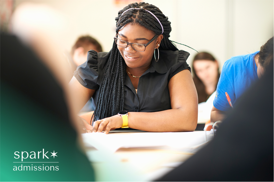 Smiling student writing in class with other students blurred in the background