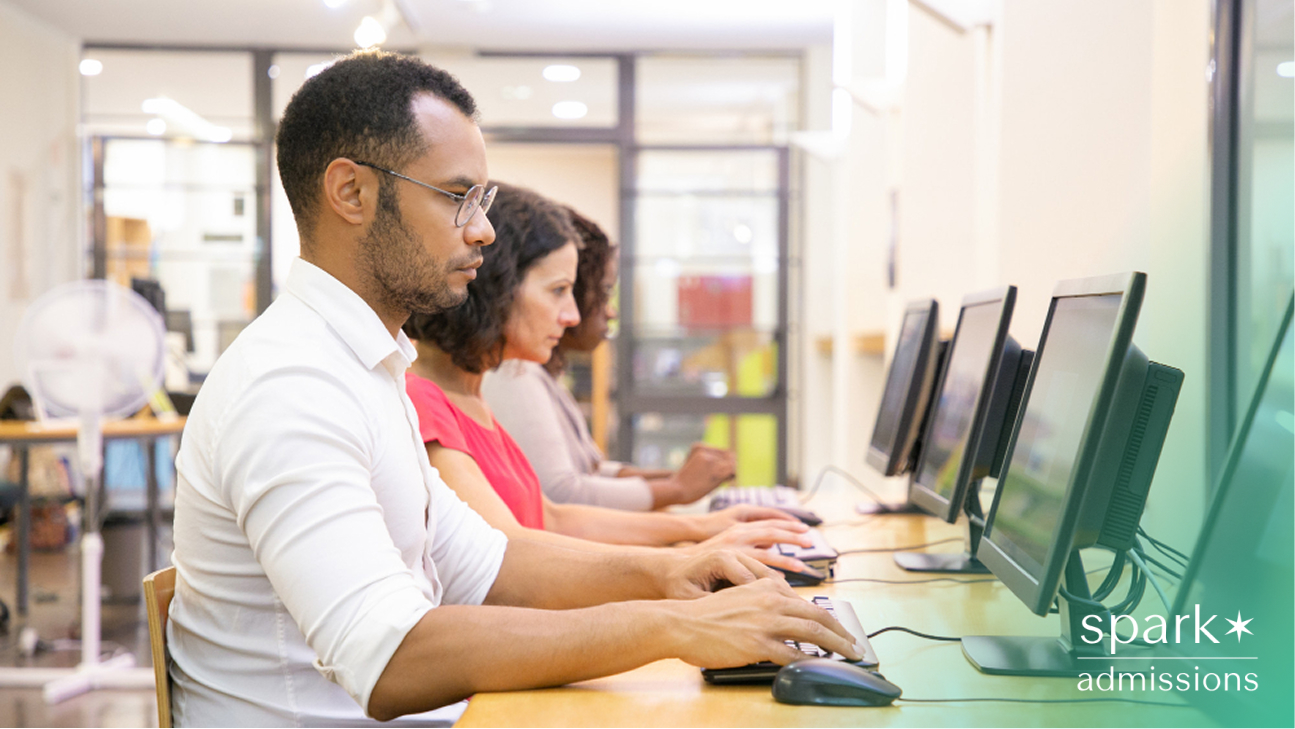 Group of adult learners focused on desktop computers in a classroom setting