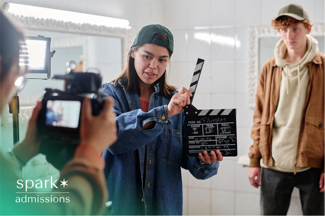 A female student holding a clapperboard on a film set, with camera and lights during a student production