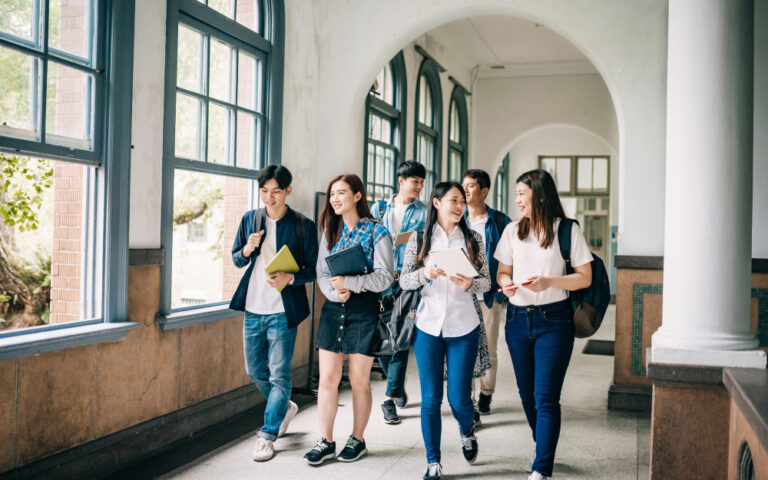 Group of students smiling and walking through a bright school hallway with backpacks