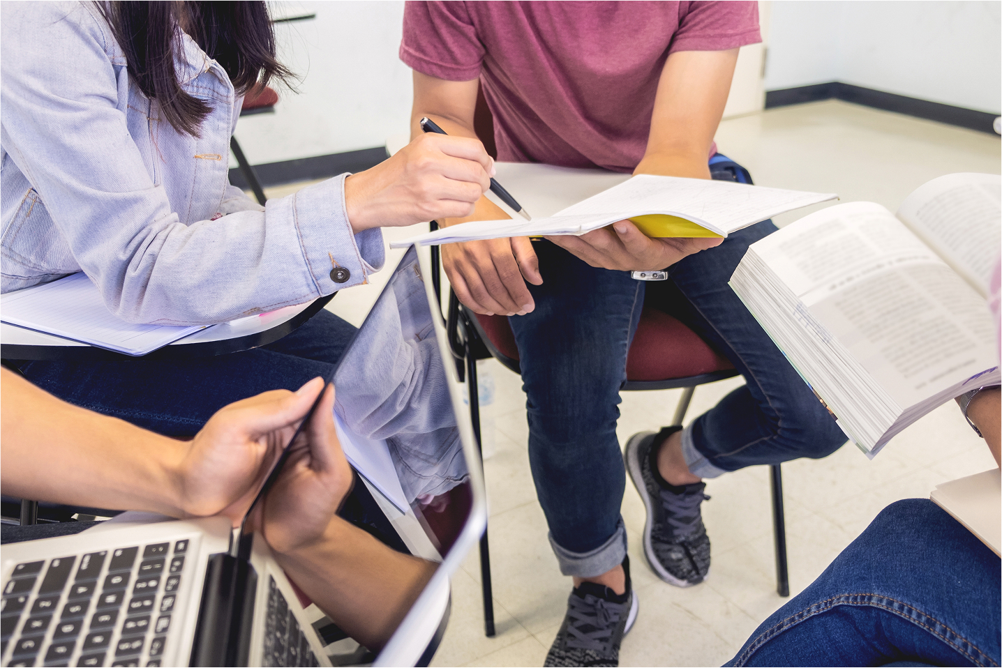 Group of students studying together with books and laptops in a classroom