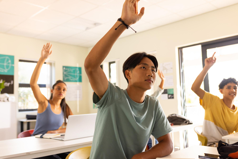 High school students raising their hands to participate in class while seated at desks.