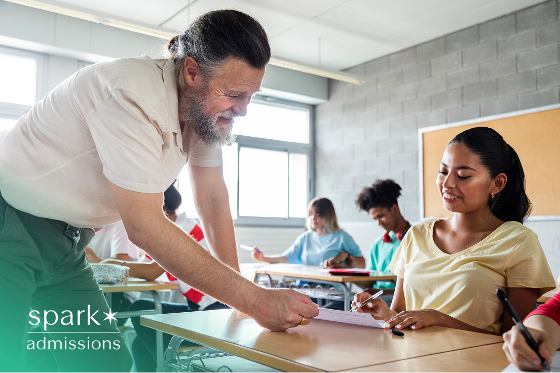 Smiling teacher assisting a student at her desk during a classroom activity