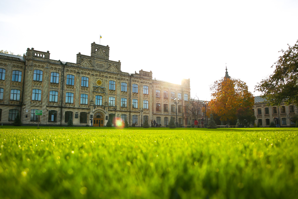 Historic university building with large windows and a green lawn lit by the sun