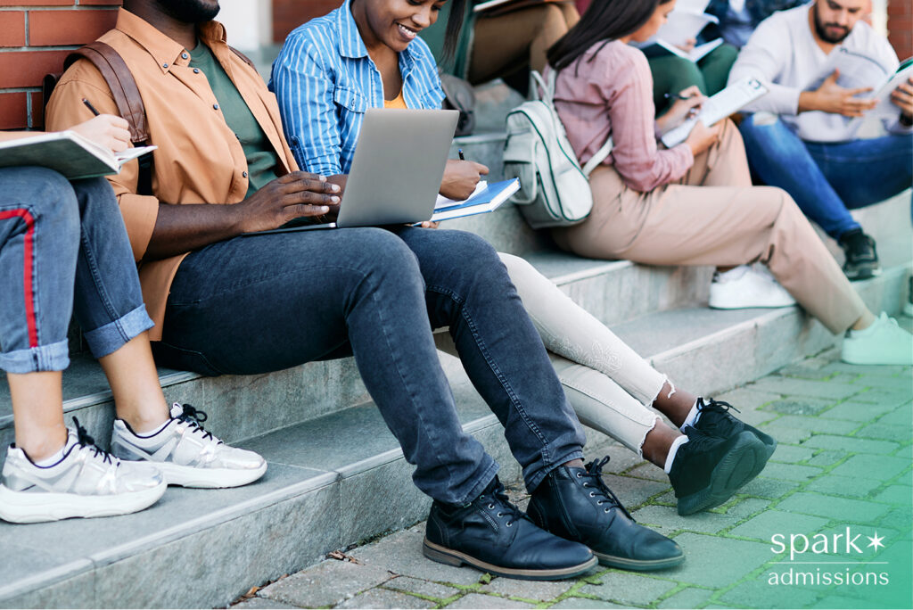 Group of college students sitting on campus steps, studying with notebooks and laptops