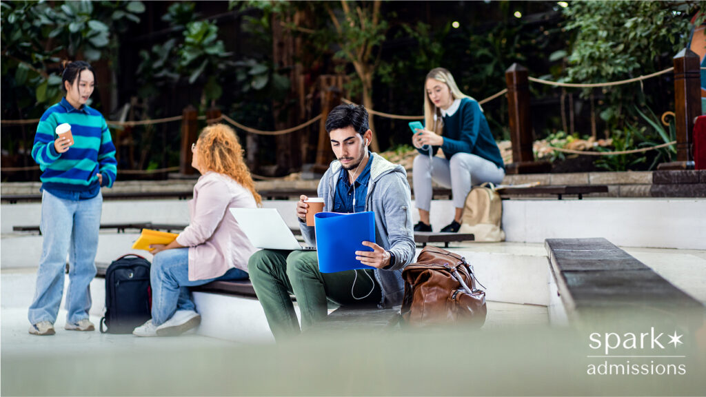 Group of college students studying outdoors, one student reviewing papers with coffee and a laptop