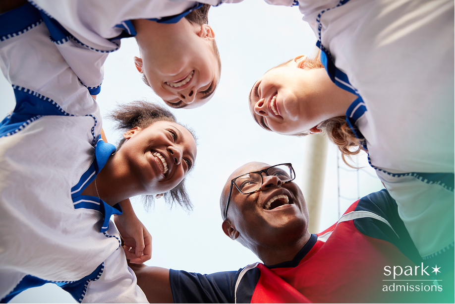 Coach and female athletes huddling and smiling during a sports practice