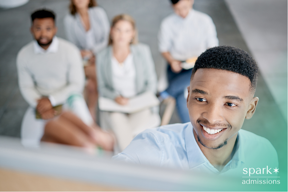 Young man student smiling while writing on a whiteboard, with classmates watching
