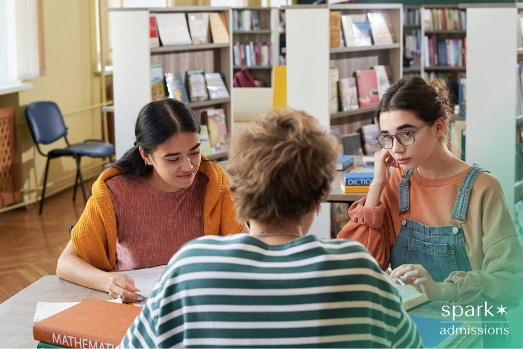 Two students talking with a counselor or tutor at a library study table