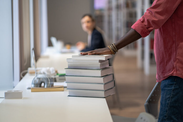 Close-up of a person placing their hand on a tall stack of books at a library table