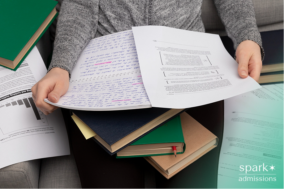 A student reviewing handwritten notes and typed pages surrounded by books and documents