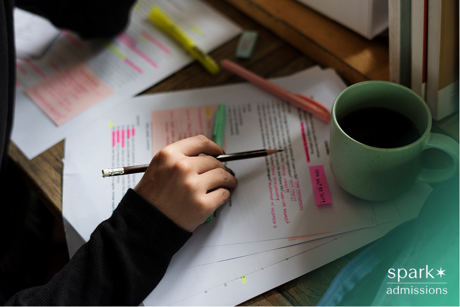 A student highlighting notes on printed pages with colorful markers next to a cup of coffee