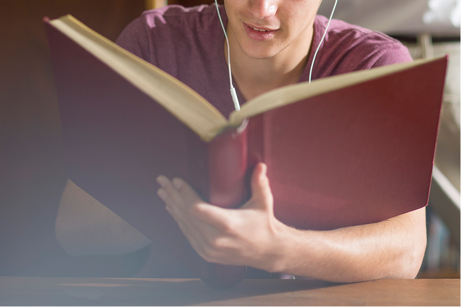 Close-up of a student reading a large red book while wearing earbuds