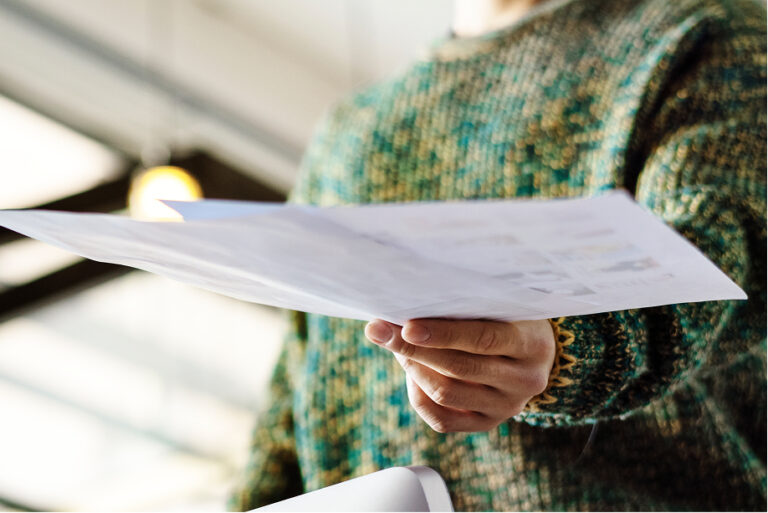 Close-up of a person in a green sweater handing over a document