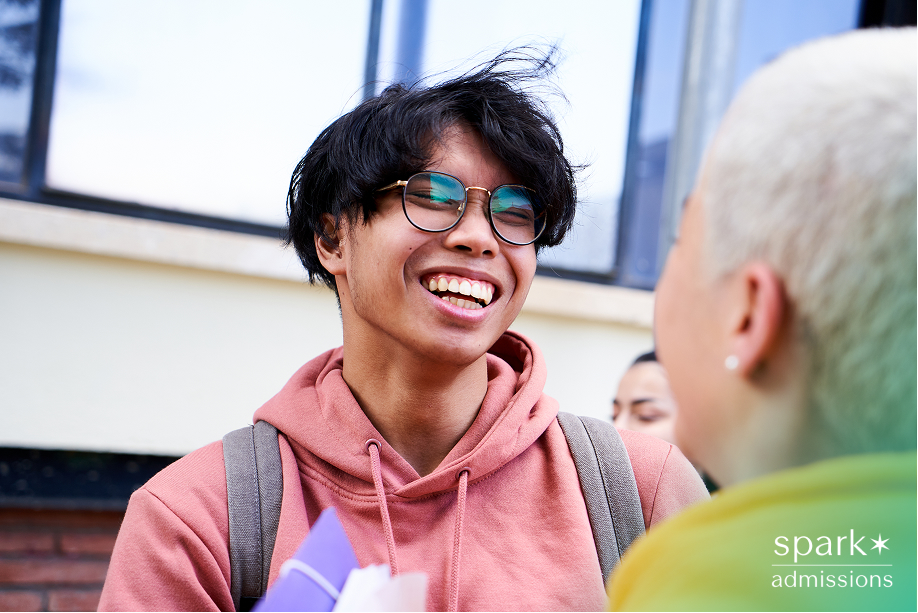 Smiling student in a pink hoodie talking with a peer outside a building