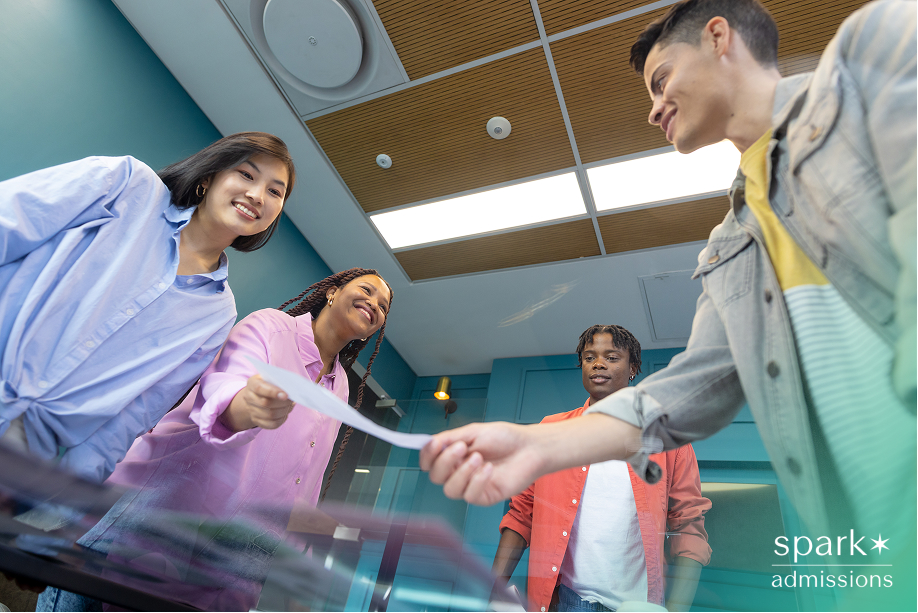 Group of students exchanging a paper in a brightly lit room with blue walls