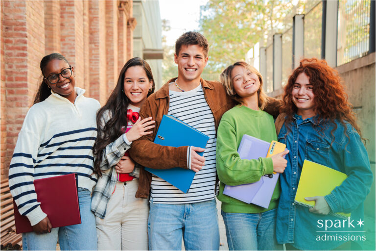 A diverse group of smiling students stands outside holding folders and notebooks