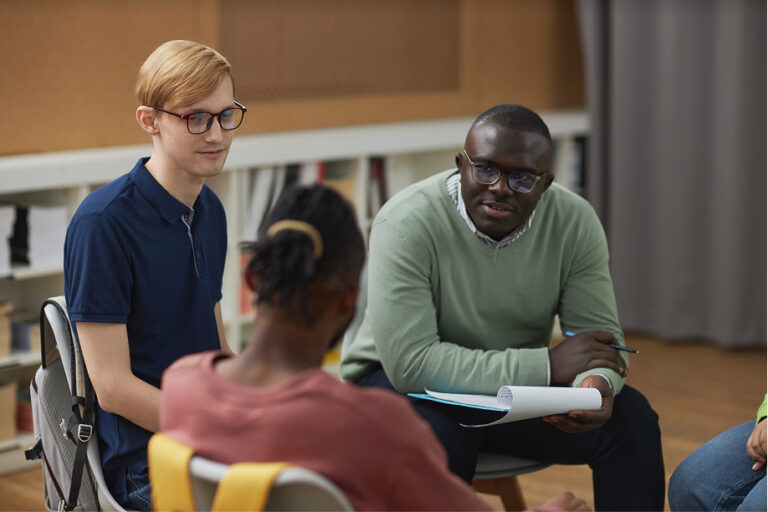 A black man as male psychologist talking to group teenagers in therapy session