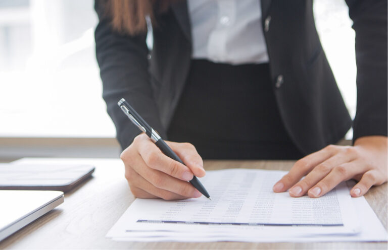A person in business attire fills out a form on a desk with a pen