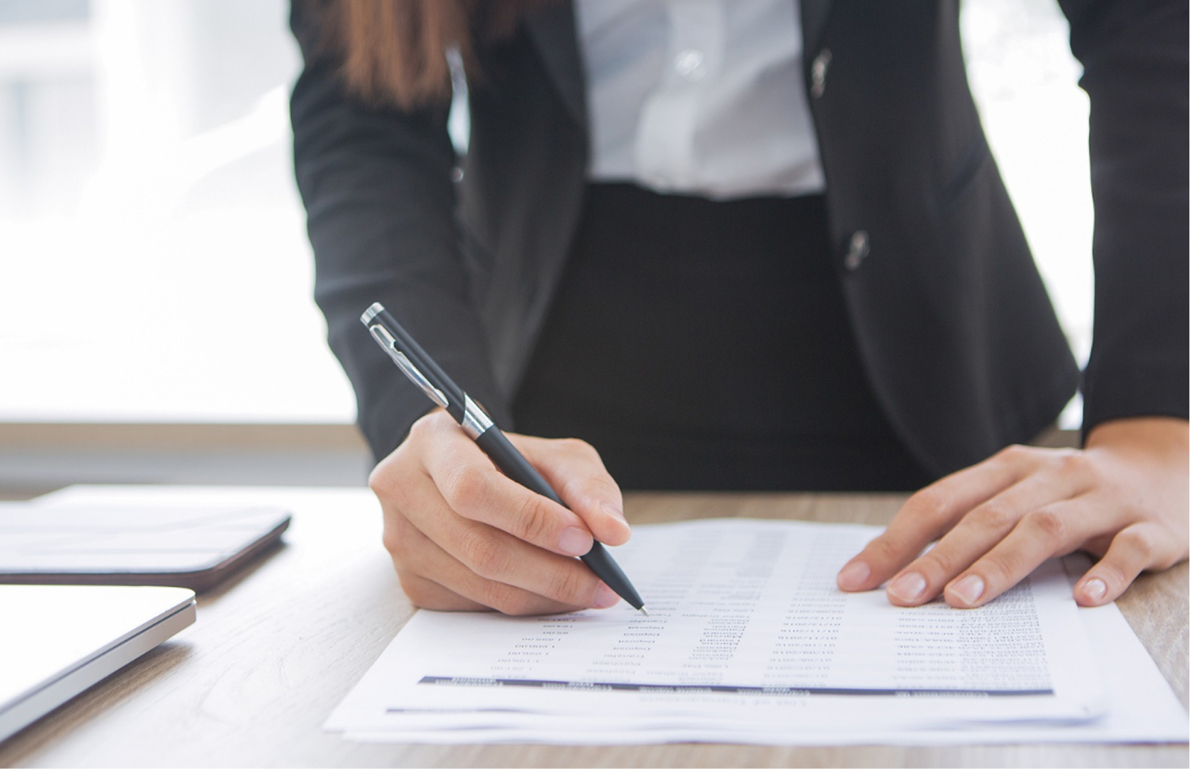 A person in business attire fills out a form on a desk with a pen