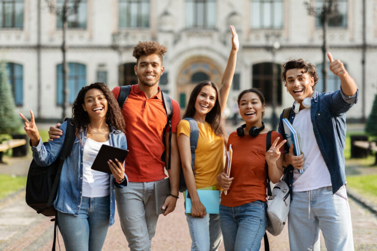 A diverse group of smiling freshman students pose outside a college building