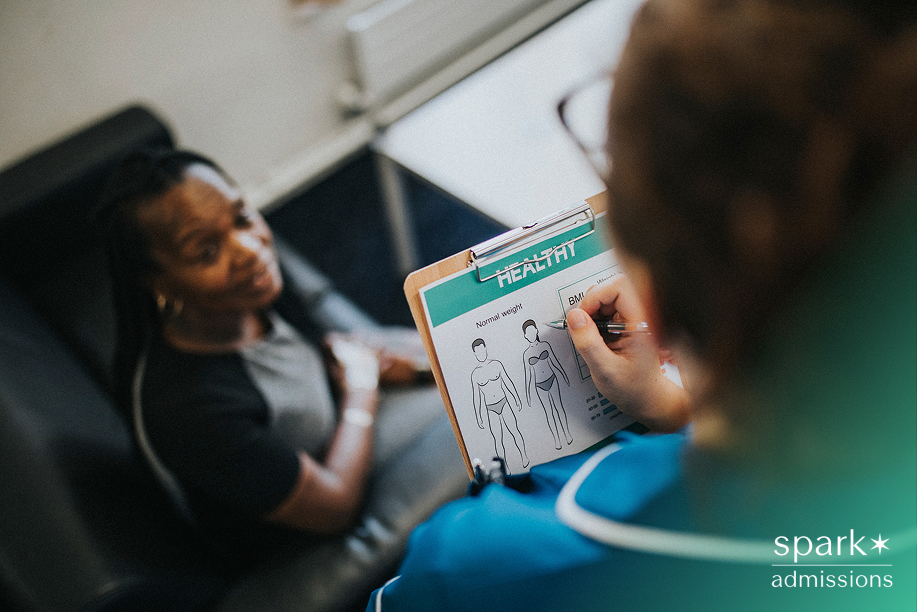 A healthcare worker shows a patient a BMI chart on a clipboard during a medical volunteer