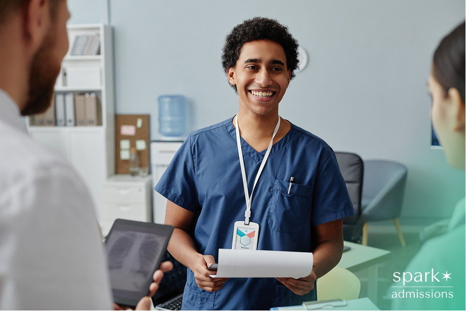 A medical student discusses a report with peers in a clinical settings, holding a clipboard as part of a medical extracurricular activity