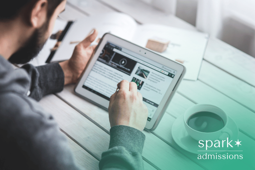 A man looking at his tablet, representing the question of whether admissions officers check applicants’ social media profiles