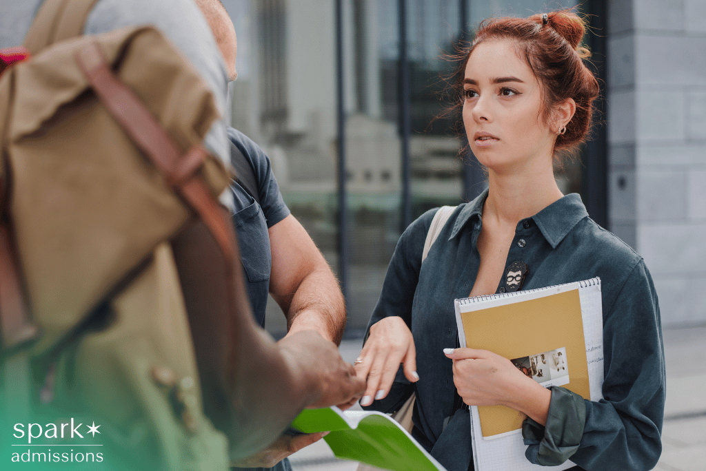 College applicant holding a large notebook while talking with peers on campus