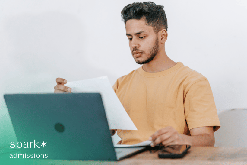 Student reviewing printed portfolio documents while using laptop