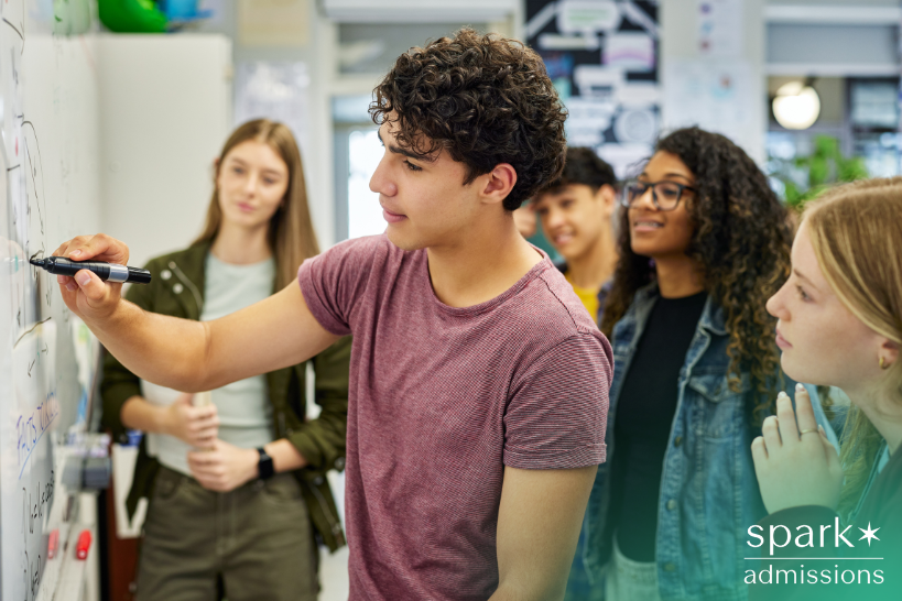 Male student solving math problem with classmates observing.
